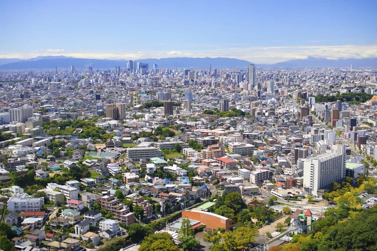 東山スカイタワーから見た晴天の名古屋市街。手前に緑の多い低層住宅地とマンション、奥に高層ビル群と山並みまで市街地が続く