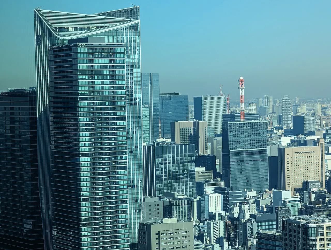高層階から見た虎ノ門ヒルズの高層タワーと周辺のオフィスビル群。奥に赤白の電波塔と都心のビルが続く