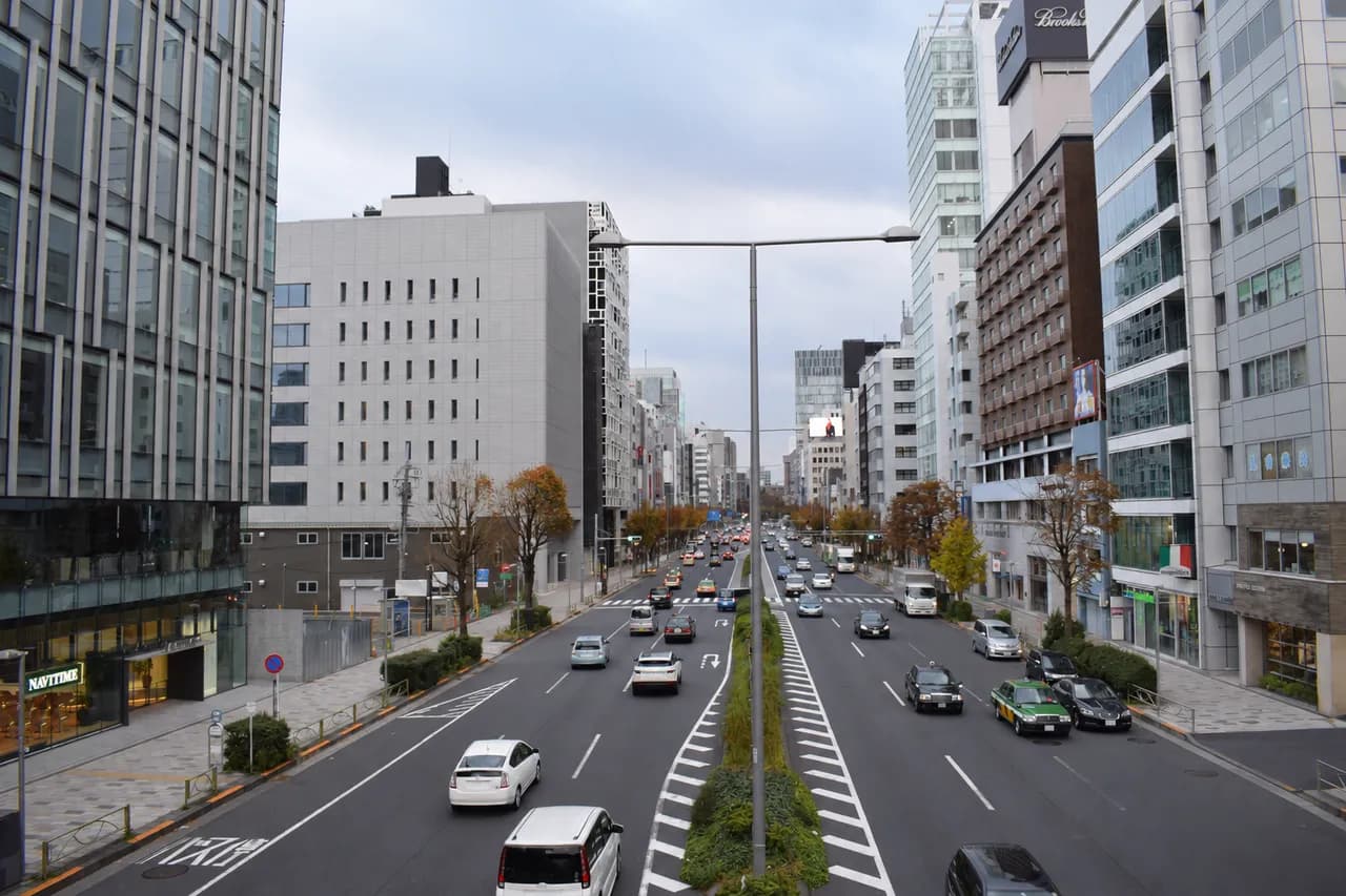 片側3車線の青山通りと両側に並ぶオフィスビル。中央分離帯に街灯と植え込みが続き、歩道沿いに街路樹が並ぶ曇り空の街並み
