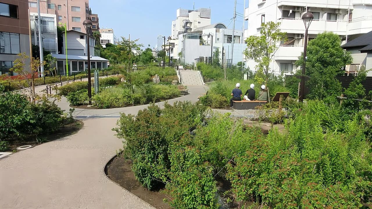 小田急線の線路跡地に整備された緑の広場。曲がりくねった散策路と植栽の奥に、中低層のマンションや住宅が並んでいる。晴天