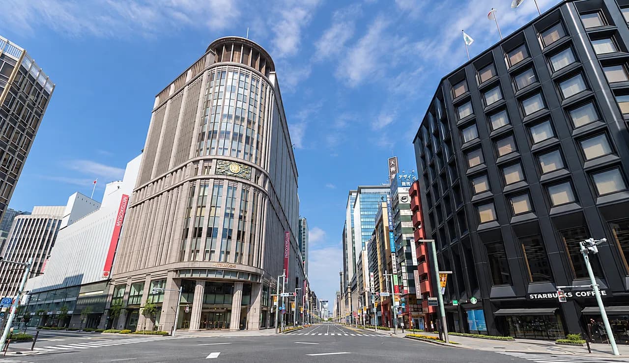 晴天の日本橋北詰交差点。左に円筒形の三越日本橋本店新館、右に黒い外壁のビル、正面の中央通りの先にオフィスビルが並ぶ