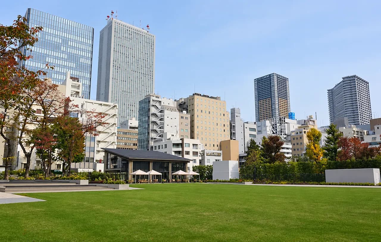 曇り空の下の南池袋公園。手前に広い芝生、奥にカフェの建物と白いテントがあり、その背後にオフィスビルや高層マンションが建ち並ぶ