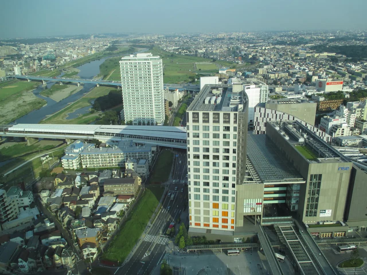 高所から見下ろした二子玉川駅周辺。駅舎とバスターミナル、商業施設と高層マンションが並び、奥に多摩川と鉄橋、川向こうの市街地が広がる