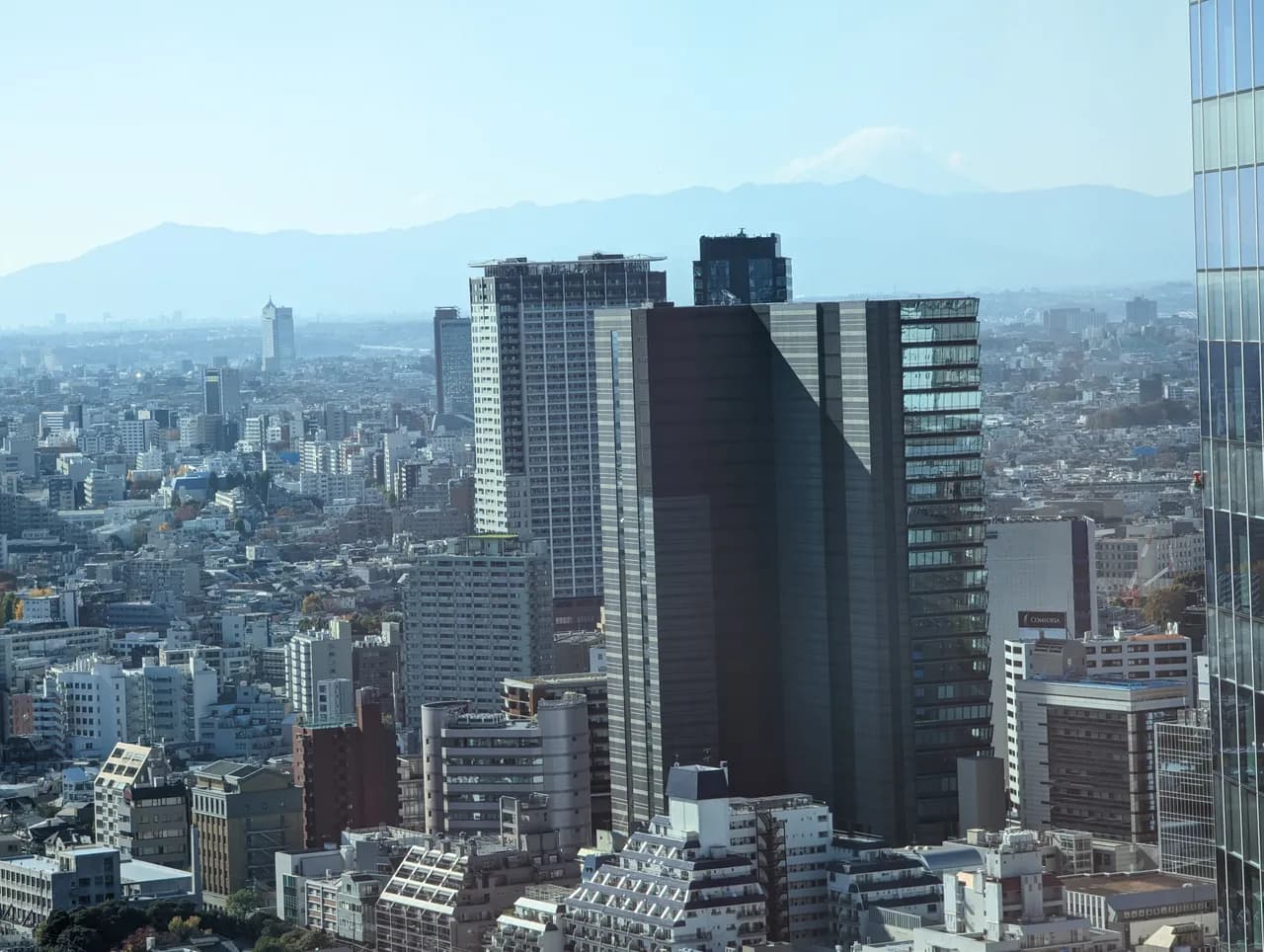 晴れた日に高い位置から見た渋谷駅の南西側。中高層のマンションやオフィスビルが密集し、中央に黒い高層ビルと白い高層マンションが建ち、奥の山並みの向こうに雪をかぶった富士山が見える