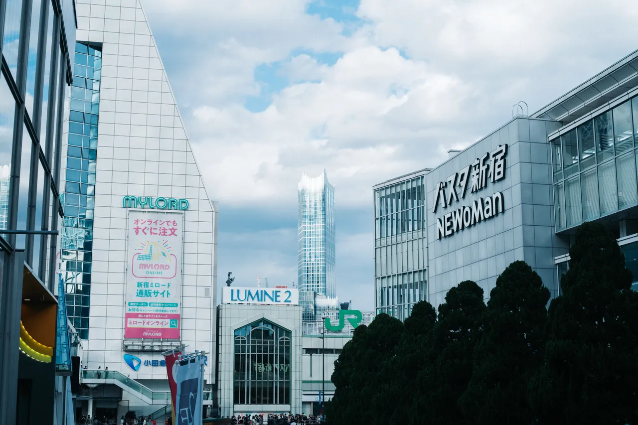 曇り空の下、新宿駅の南口に向かう眺め。右にバスタ新宿とNEWoManの駅ビル、正面奥にルミネ2の建物と高層ビル、左に小田急の駅ビルが並ぶ